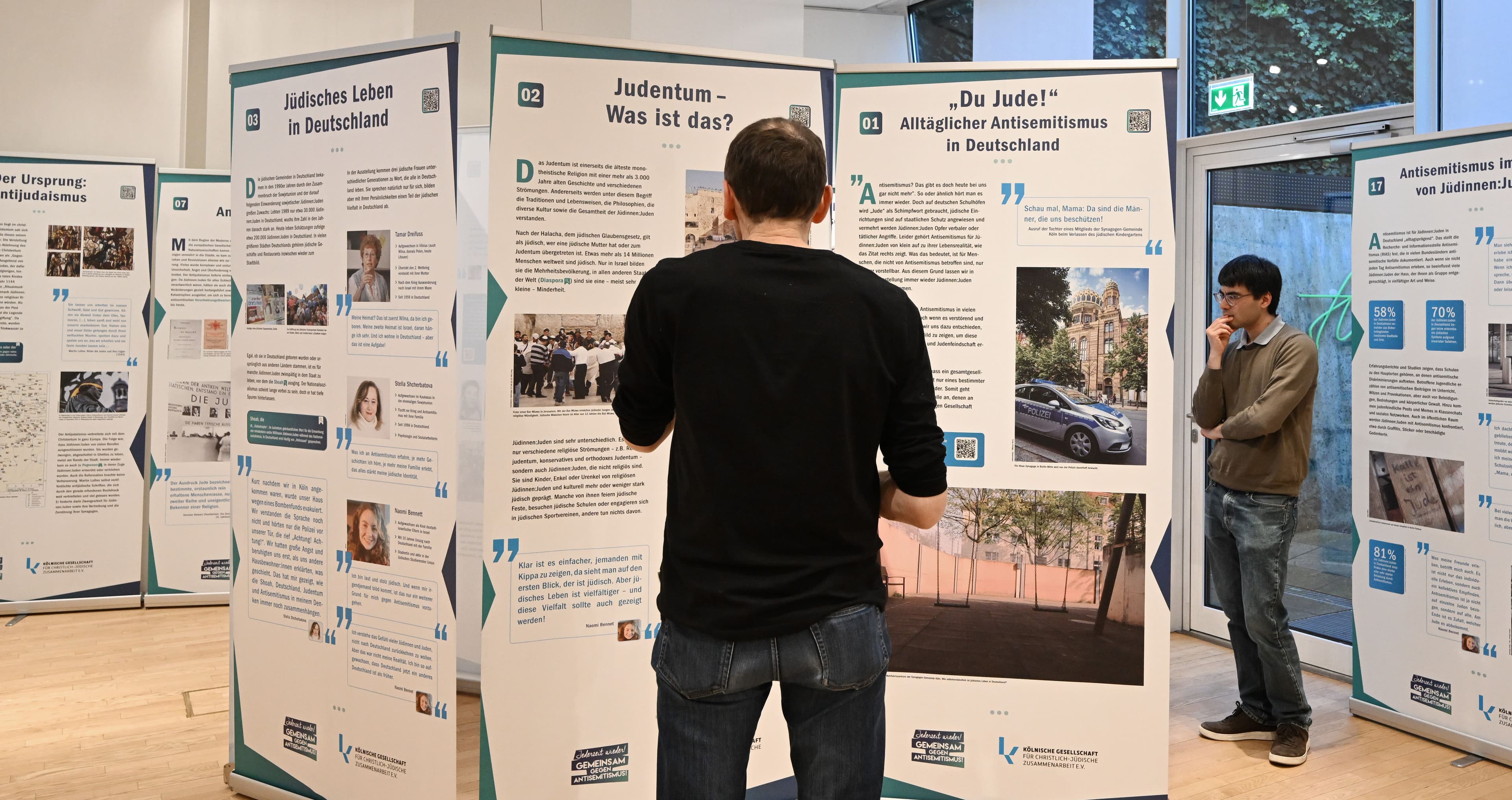 Besucher schauen sich Plakate zum Thema "Jüdisches Leben" und "Judentum" an.