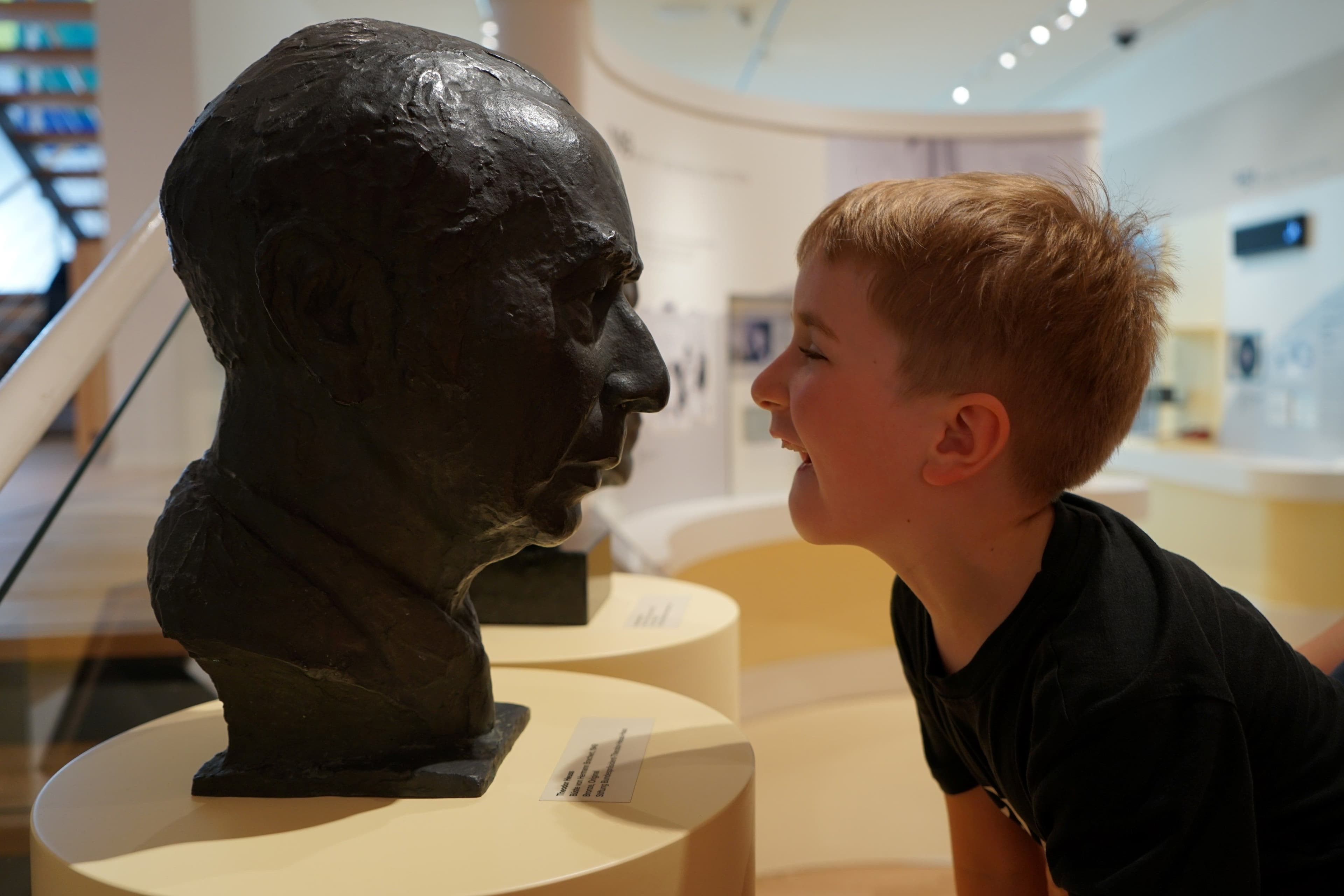 Ein Junge lacht die Büste von Theodor Heuss in der Ausstellung an.